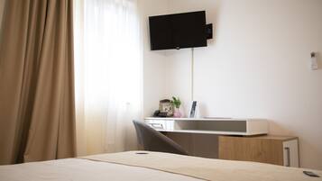 A hotel room with a bed, a desk with a computer, a chair, a TV mounted on the wall, and a small cabinet.