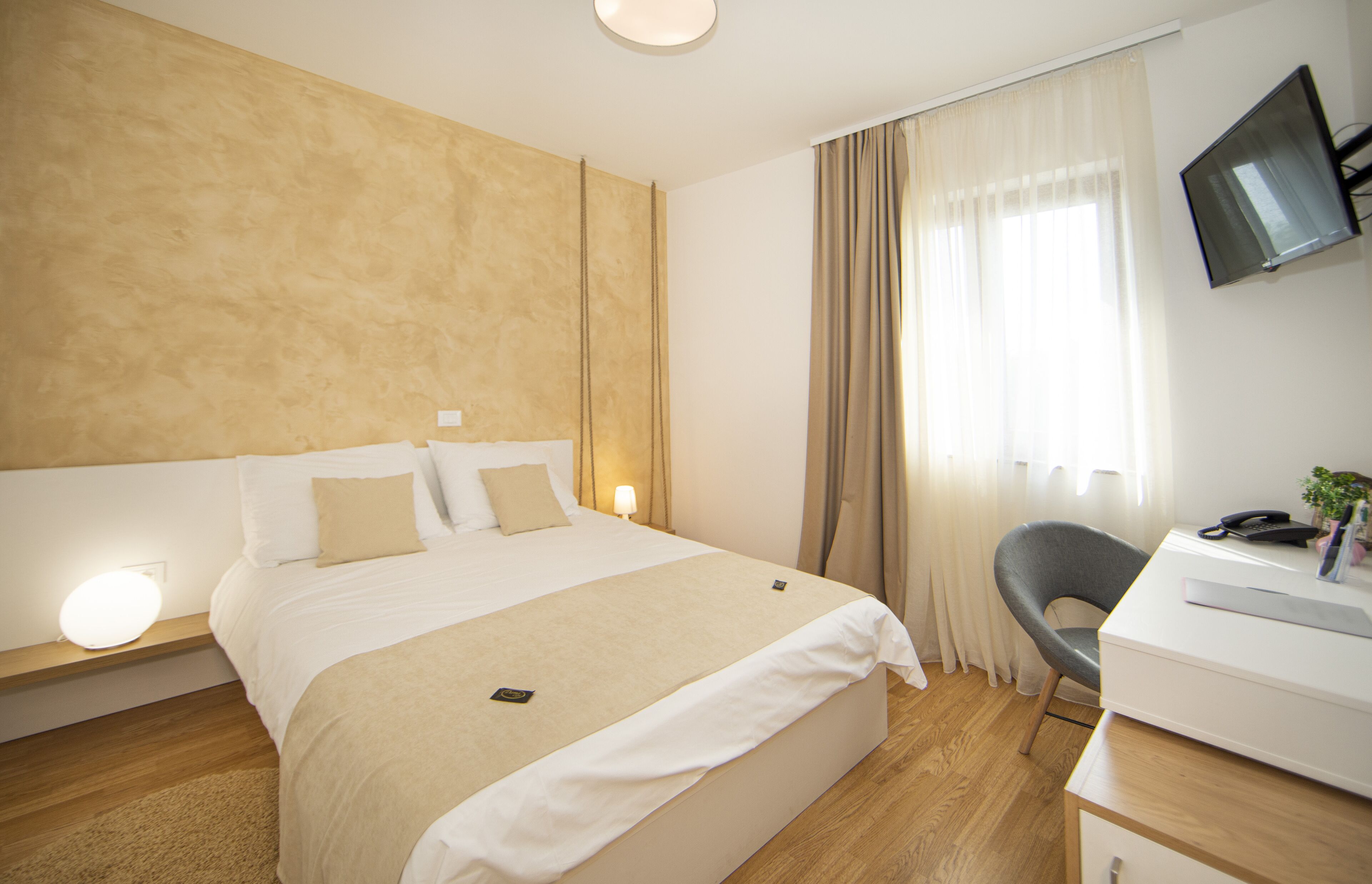 Een hotelkamer met een groot bed, een bedlampje, een bureau, een stoel en een televisie aan de muur.