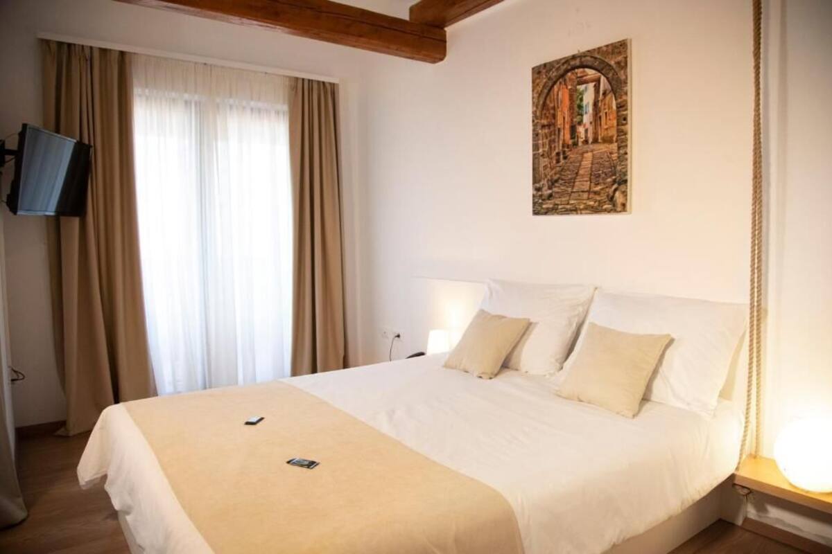 A hotel room with a large bed, beige curtains, a mounted TV, and a painting on the wall.