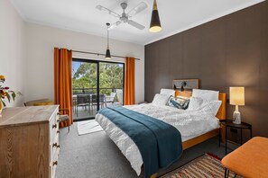 A hotel room with a bed, a desk, a chair, a lamp, a ceiling fan, and a view of the outdoors through a sliding door. - Blue Haven at Aireys (Aireys Inlet)