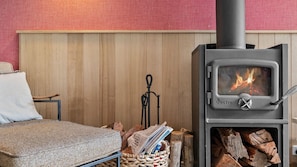 Une pièce chaleureuse avec un poêle à bois, un lit et un panier de bois de chauffage.