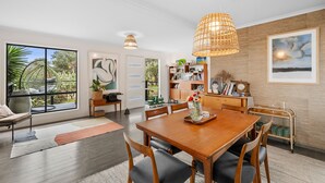 A dining area with a wooden table and chairs, a bookshelf, and a large window with a view of greenery. - Blue Haven at Aireys (Aireys Inlet)