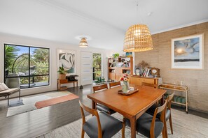 A dining area with a wooden table and chairs, a bookshelf, and a large window with a view of greenery. - Blue Haven at Aireys (Aireys Inlet)