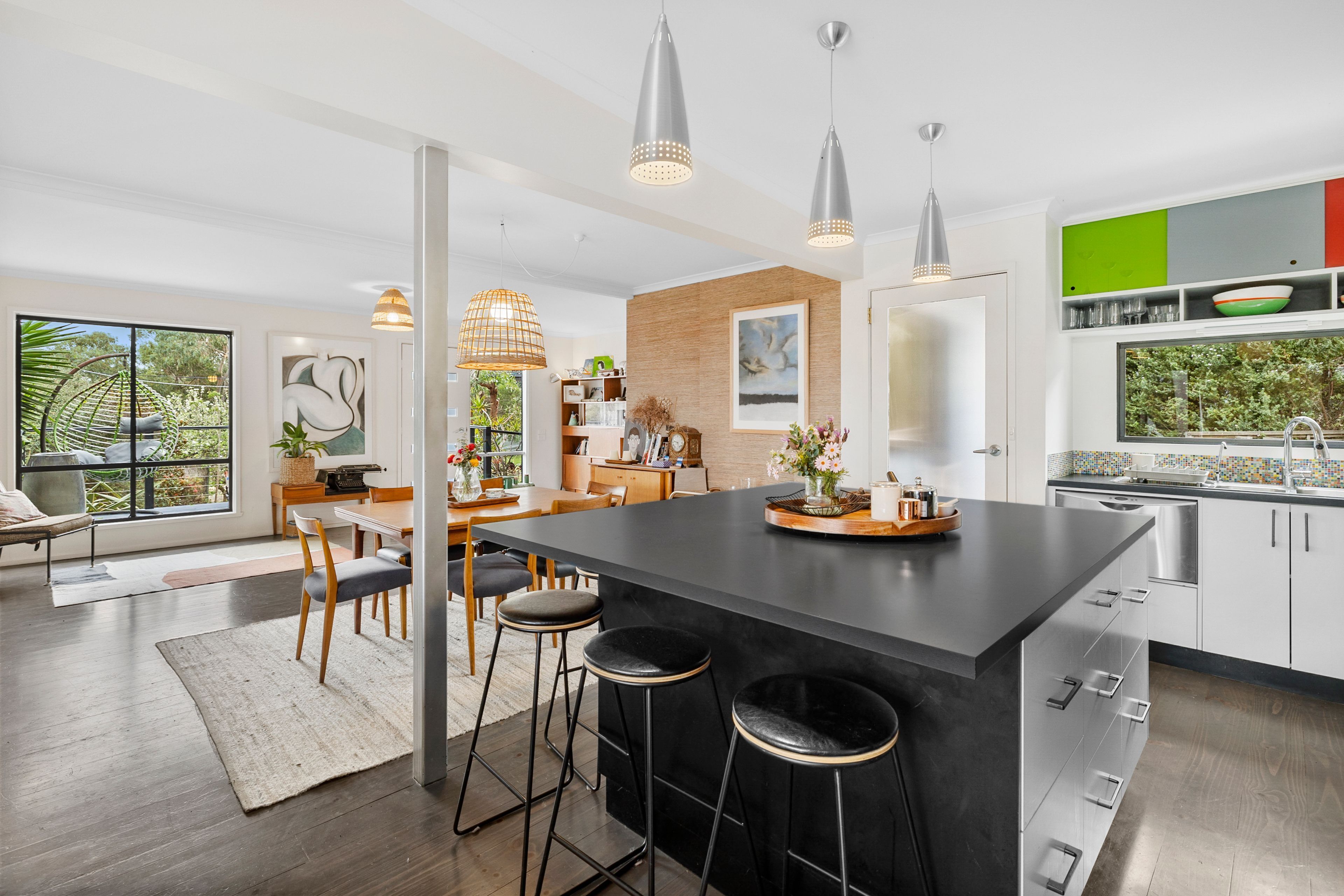 A modern kitchen with a central island, bar stools, pendant lighting, and a view of the outdoors.