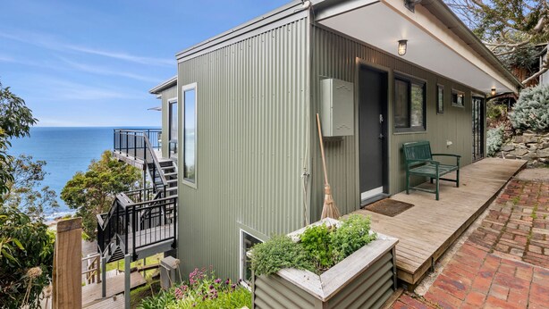 A coastal property with a metal exterior, a wooden deck, a green chair, and a view of the sea.