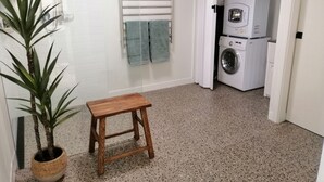 A bathroom with a washing machine, a towel rack, and a small wooden stool.