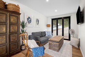 A living room with a grey sofa, wicker furniture, a large cabinet, and artwork on the wall.