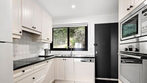 A modern kitchen with white cabinetry, a black countertop, and stainless steel appliances including a Bosch oven and microwave.