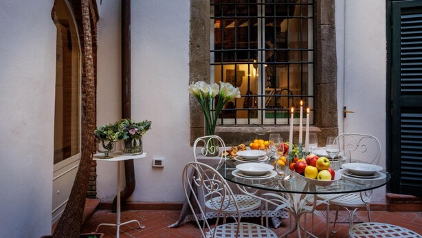 A glass table set for dining with chairs, a window with bars, and a door. - Casa Al Dipinto in Lucca (Lucca)