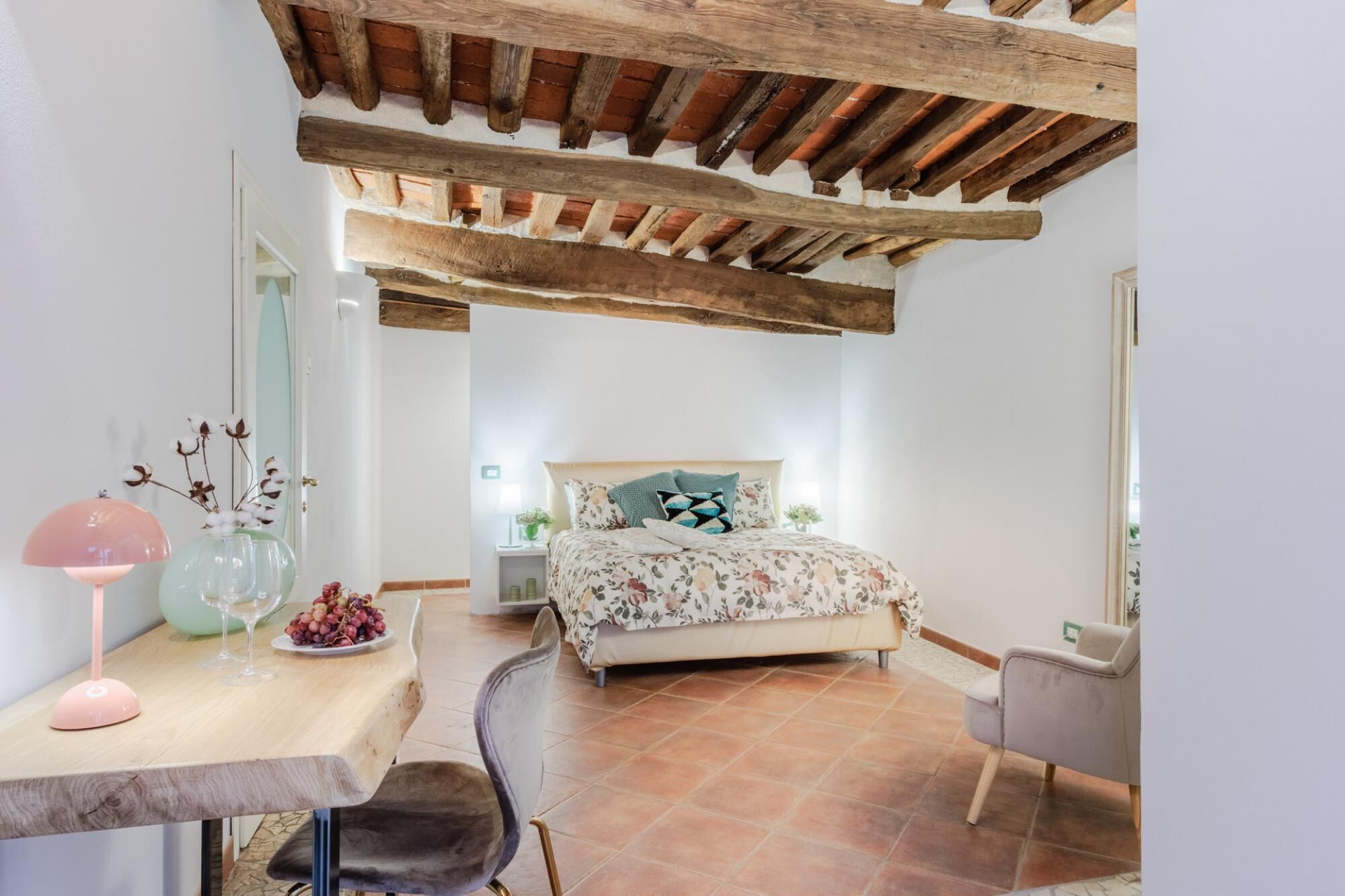 A bedroom with a bed, a desk, a chair, and a table with a lamp and a vase.