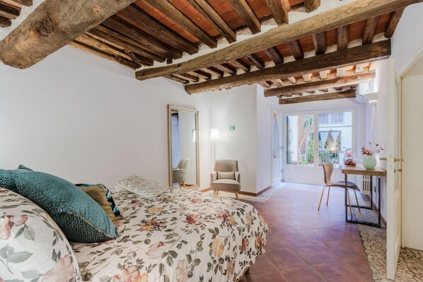 A bedroom with a wooden ceiling, a floral bedspread, and a view to a balcony with a table and chairs. - Casa Al Dipinto in Lucca (Lucca)