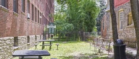 Un patio con mesas de picnic, un letrero de parque canino y un edificio de piedra.