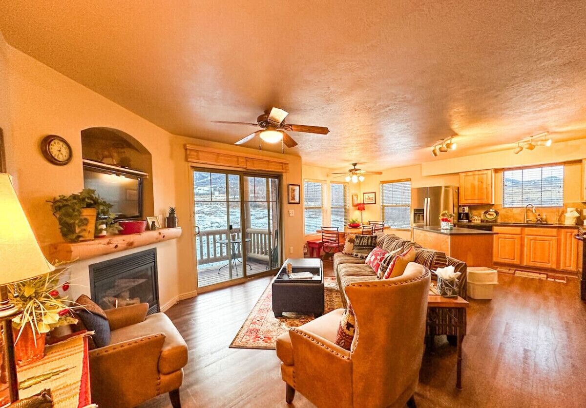 A spacious living room with a fireplace, a dining area, and a kitchen. There is a large window providing a view of the outdoors.