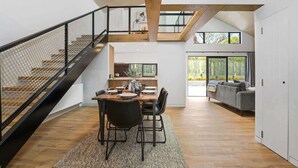A modern interior with a dining area, staircase, and a living space with a sofa and large windows. - Serenity on Sophia - Spa Pool, Sleeps 6 (Rotorua)