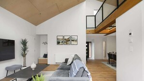 A modern living room with a grey sofa, a coffee table, and a TV mounted on the wall. There is a staircase leading to an upper level. - Serenity on Sophia - Spa Pool, Sleeps 6 (Rotorua)