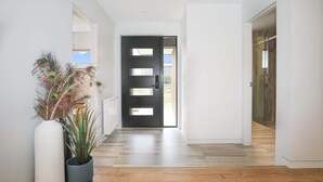A modern hallway with a black door, wooden flooring, and a potted plant. - Serenity on Sophia - Spa Pool, Sleeps 6 (Rotorua)