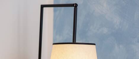 A modern table lamp with a cylindrical shade on a wooden surface against a blue wall.