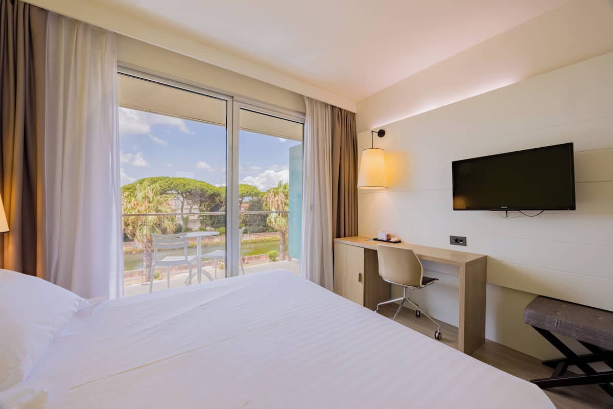 Une chambre d’hôtel équipée d’un lit, d’un bureau, d’une chaise, d’une télévision et d’un balcon donnant sur un paysage verdoyant.