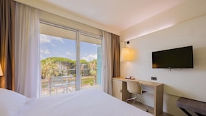 A hotel room with a bed, a desk, a chair, a TV, and a balcony with a view of greenery. - Hotel Viareggio (Viareggio)