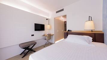 Una habitación de hotel moderna con una cama grande, un escritorio, una silla, un televisor y dos lámparas fijadas a la pared.