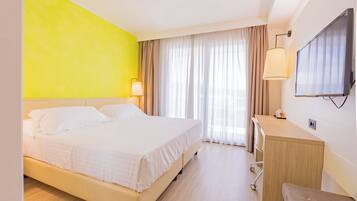 Ein Hotelzimmer mit Bett, Schreibtisch, Fernseher und einem Fenster mit Vorhängen.