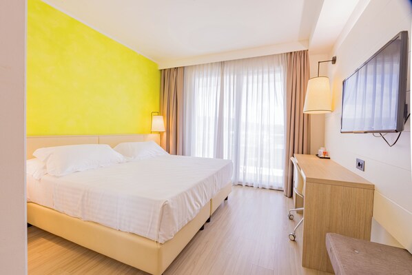 Une chambre d’hôtel avec un lit, un bureau, une télévision et une fenêtre avec des rideaux.