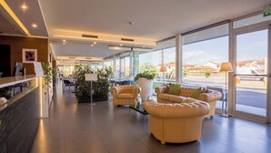 A modern hotel lobby with leather sofas, a reception desk, and large windows offering a view of the city. - Hotel Viareggio (Viareggio)
