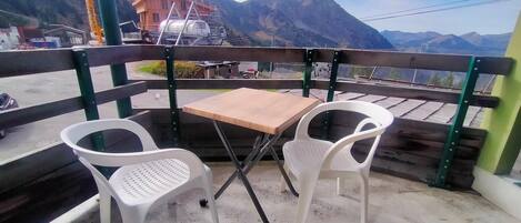 Un balcón con una mesa y dos sillas, con vistas a un paisaje montañoso y una obra en construcción al fondo.