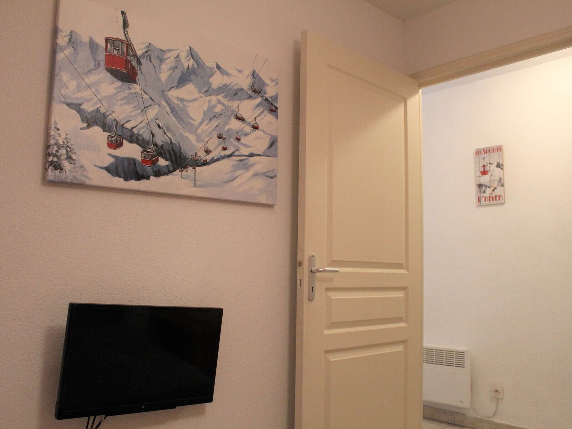 A room with a wall-mounted TV, a door, and a poster.