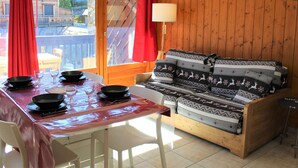 Una stanza accogliente con parete in legno, un divano con cuscini decorati, un tavolo da pranzo con ciotole nere e una tenda rossa.