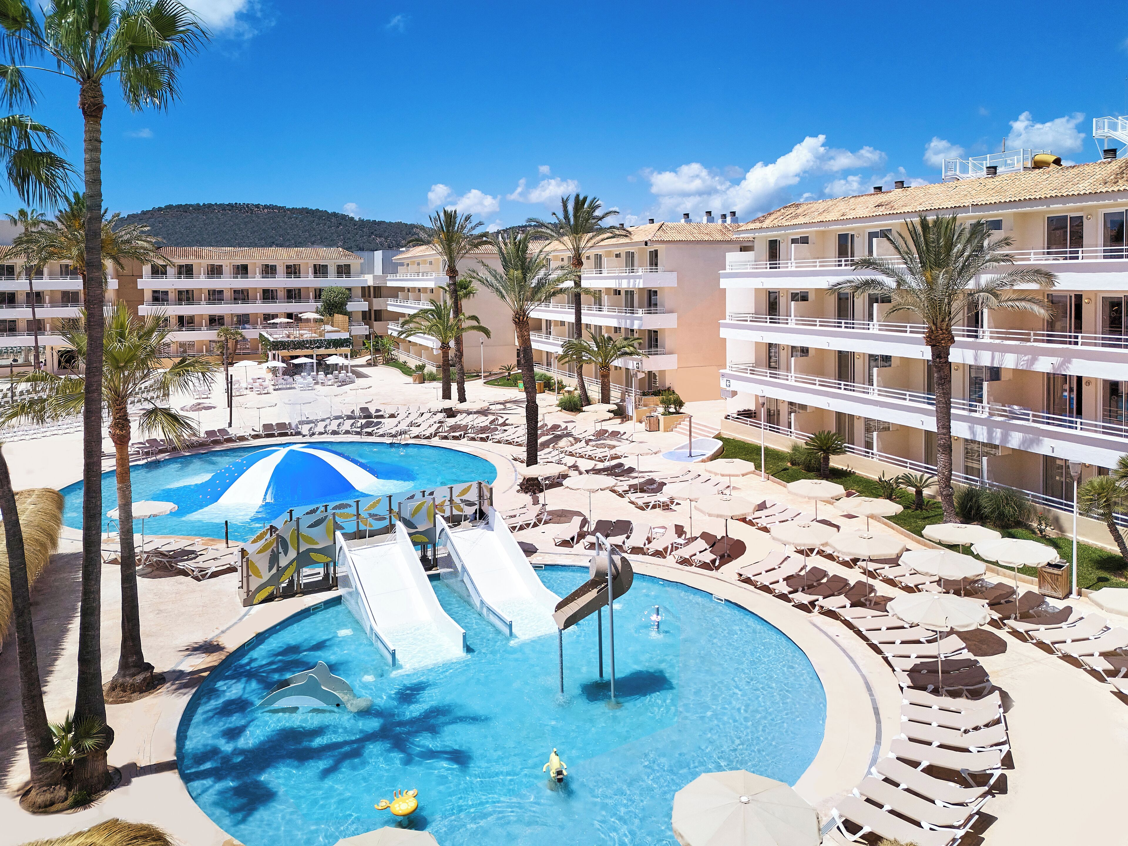 A resort with multiple swimming pools, palm trees, and a mountainous backdrop.