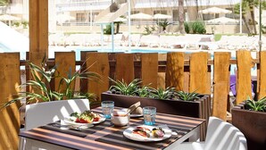 A dining area with tables and chairs, a pool in the background, and potted plants. - FERGUS Club Mallorca Waterpark (Calvia)