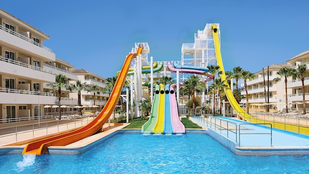 A swimming pool with multiple colorful water slides and a poolside area with lounge chairs and palm trees. - FERGUS Club Mallorca Waterpark (Calvia)