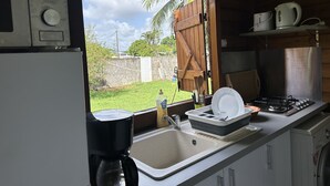A kitchen with a window, a coffee maker, a sink, and a stove. - Appart Bellissima Calme Paisible Entouré de Verdure (Baie-Mahault)