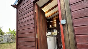 A wooden building with a kitchen area visible through an open door. - Appart Bellissima Calme Paisible Entouré de Verdure (Baie-Mahault)