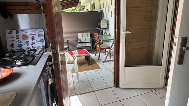 A kitchen with a gas stove, a microwave, and a refrigerator. There is a dining area with a table and chairs. - Appart Bellissima Calme Paisible Entouré de Verdure (Baie-Mahault)