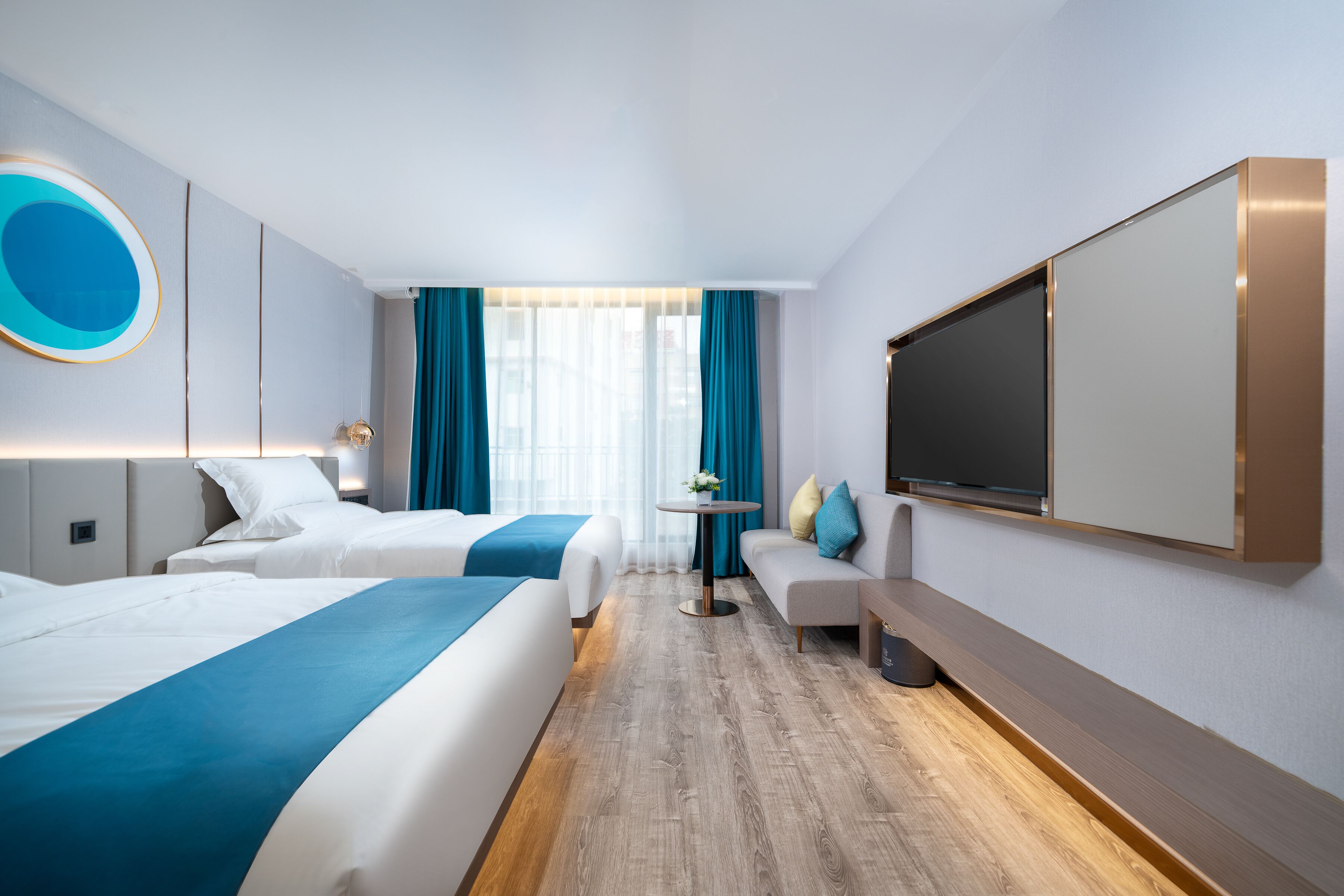 Una camera d'albergo con due letti, una televisione, un tavolino con un fiore e un divano.