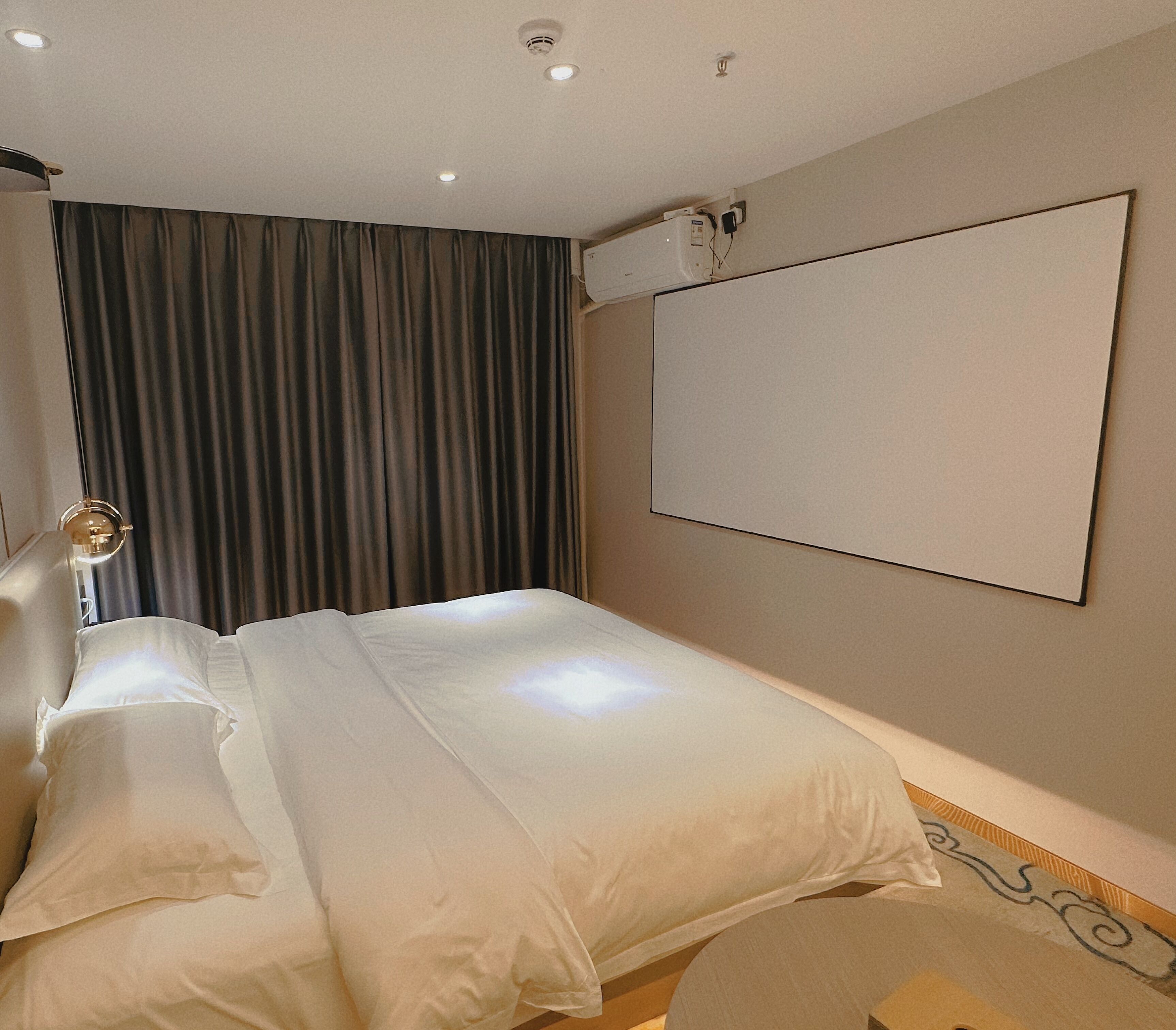 Ein Hotelzimmer mit Bett, Vorhängen, einem an der Wand befestigten Fernseher und einer Deckenleuchte.