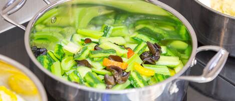 Une casserole en acier inoxydable sur une cuisinière, avec divers légumes.