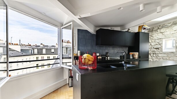Une cuisine moderne dotée d’un grand îlot central, de meubles de rangement aux couleurs sombres et d’un mur d’accent en pierre.