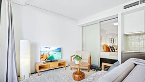 Quarto de hotel moderno com uma cama grande, uma televisão, uma mesinha com uma planta e uma porta deslizante para um banheiro.