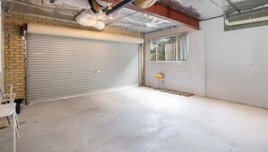 A garage with a closed roller door, a window, and a concrete floor. - Seaside Serenity-Panoramic Water Views-Sleeps 9. (Sandy Bay)