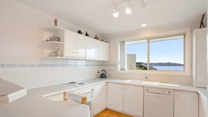 Een moderne keuken met witte kastjes, een houten visgraatvloer, een groot raam met uitzicht en een waterkoker op het aanrecht.