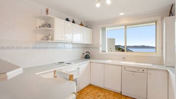 A modern kitchen with white cabinetry, a wooden herringbone floor, a large window with a view, and a kettle on the counter.