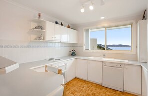 A modern kitchen with white cabinetry, a wooden herringbone floor, a large window with a view, and a kettle on the counter.