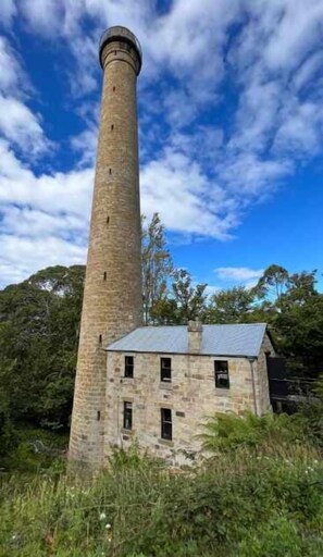 A tall stone tower with a metal roof, surrounded by greenery.
