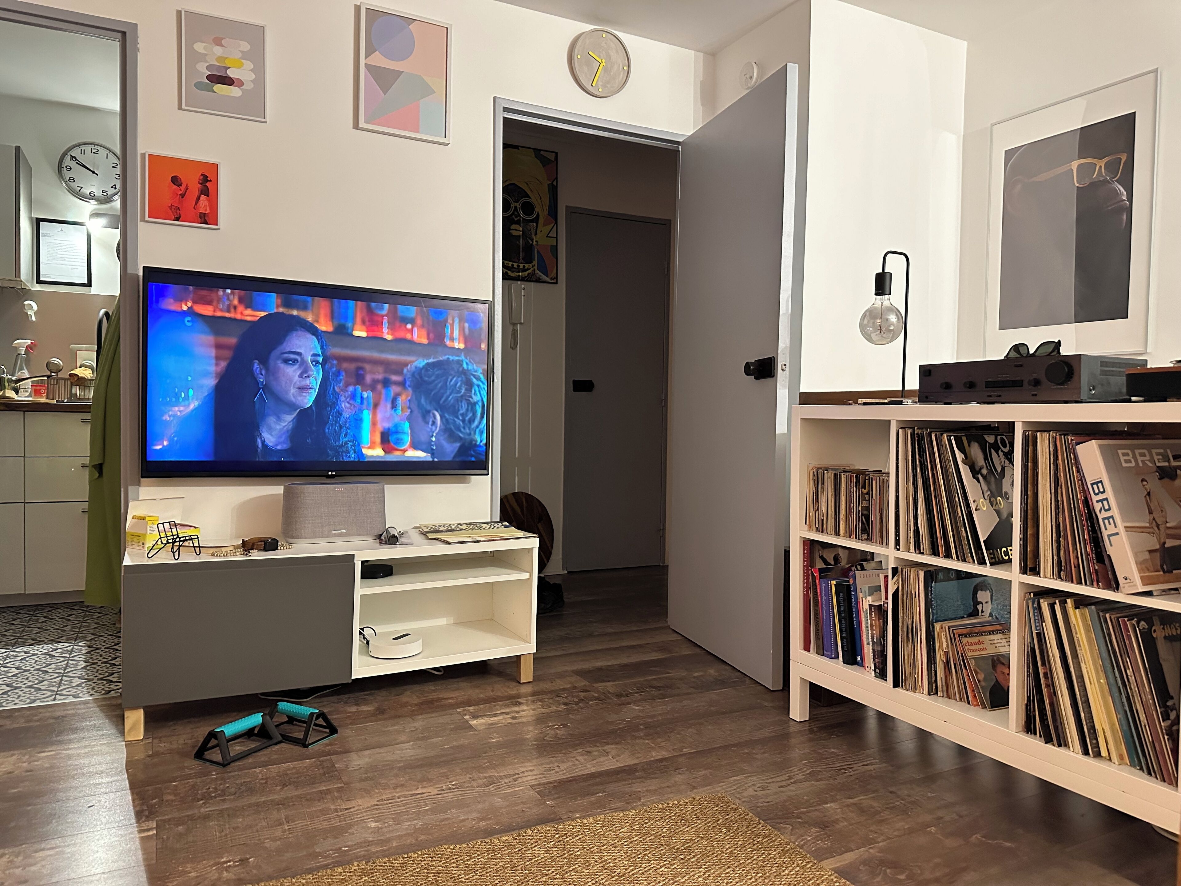 A living room with a flat-screen TV, a bookshelf filled with vinyl records, and a door leading to another room.