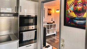 Una cocina moderna con electrodomésticos de acero inoxidable, un armario blanco y un colorido cuadro abstracto en la pared.