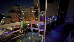 Un balcón exterior de varios niveles con una escalera espiral, plantas en macetas y luces colgantes.