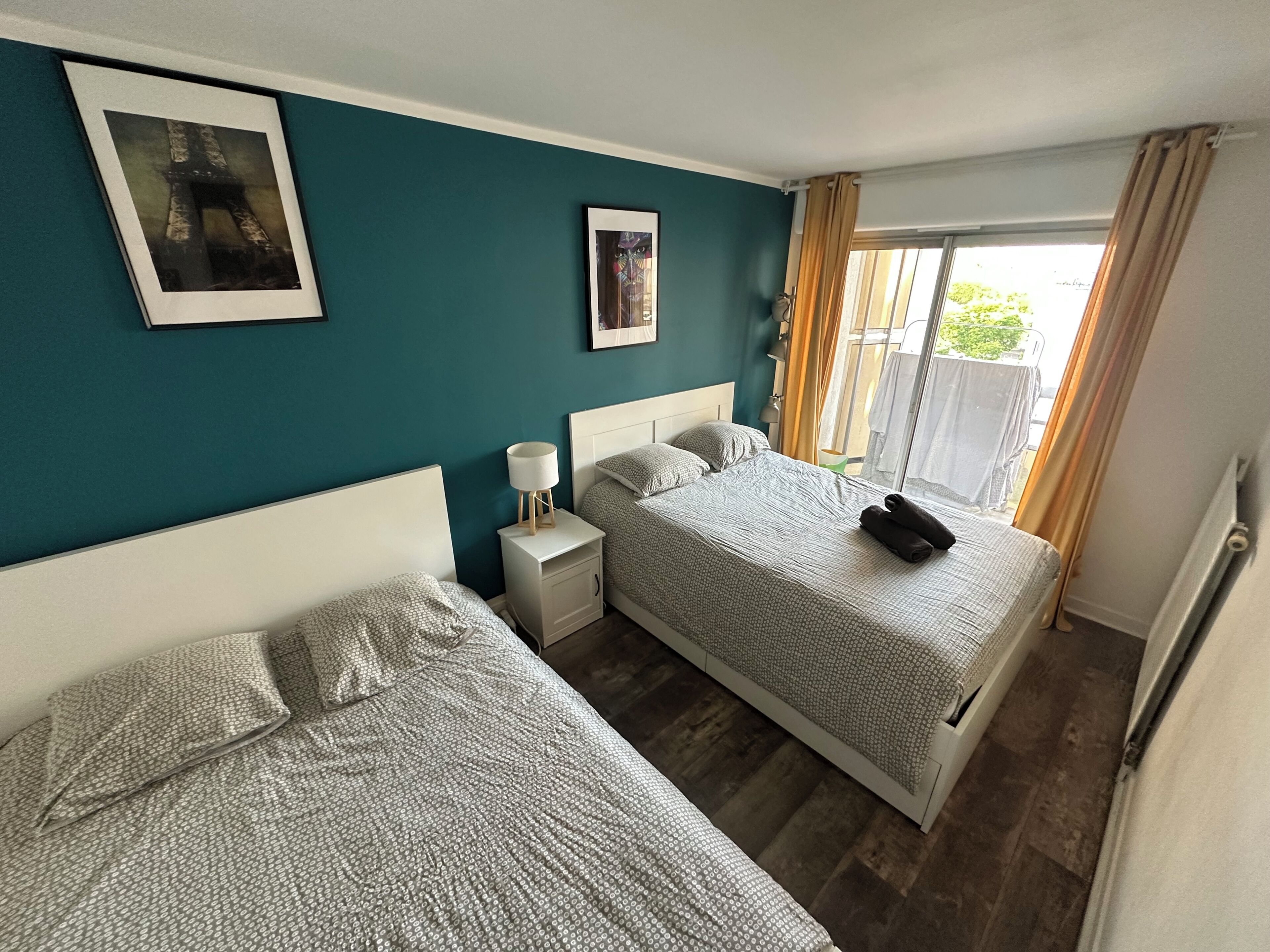 Une chambre d’hôtel avec deux lits, une table de chevet avec une lampe, une fenêtre avec des rideaux et une vue sur la verdure.